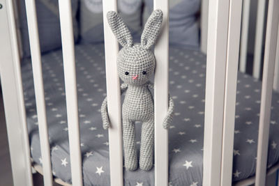 Grey knitted rabbit sitting behind the partitions in bed