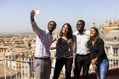 Happy multi-ethnic colleagues taking selfie at office rooftop during break