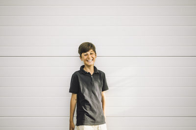 Portrait of happy boy standing against white wall