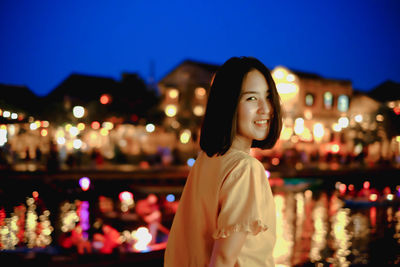 Portrait of smiling woman standing against illuminated sky at night