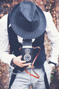 Mature man photographing while standing against brick wall during autumn