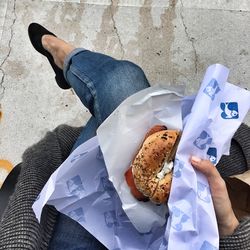 Low section of woman holding burger while sitting outdoors