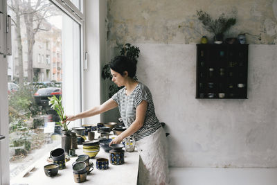 Side view of woman using mobile phone while standing against wall