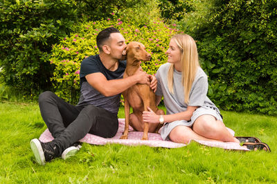 Couple and vizsla dog relaxing on grass