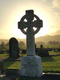 Cross in cemetery against sky during sunset