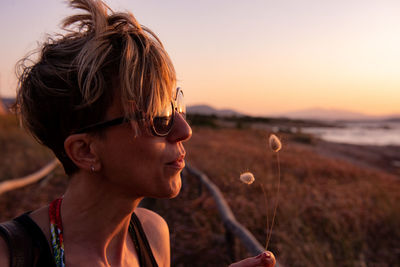 Close-up of mature woman blowing dandelion on field