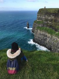 Rear view of woman sitting by sea against sky