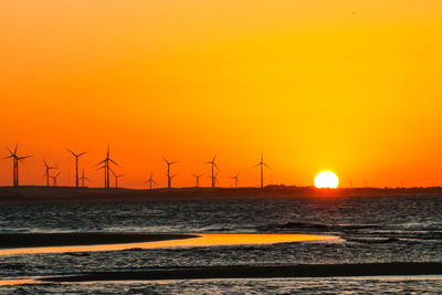 Sea by windmills against clear sky during sunset