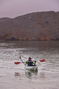 Man rowing boat in river against mountains