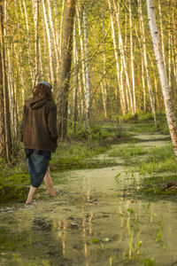 Rear view of woman walking in swamp against trees at forest