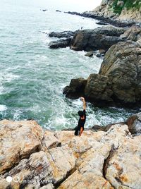 Woman standing on cliff by sea against sky