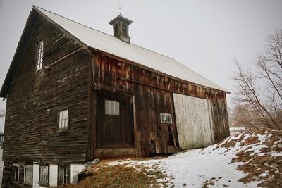 Abandoned house on snow covered field against sky