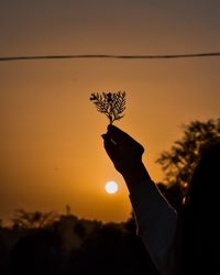 Close-up of silhouette hand holding sun during sunset