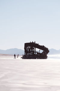 Silhouette person in abandoned boat on shore against clear sky