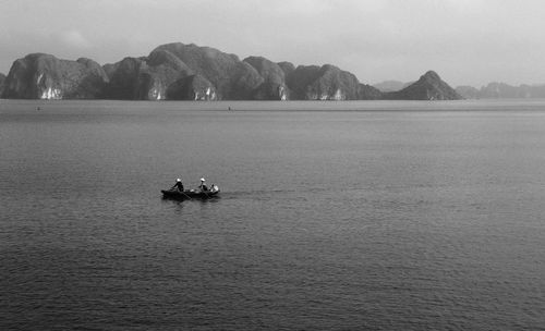 People in boat sailing on sea against mountains