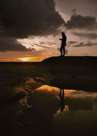 Silhouette man standing on shore against sky during sunset