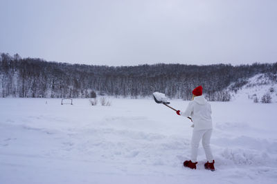 A woman in a white suit cleans snow on the street