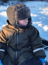 Child looking away while sitting in snow