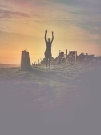Silhouette of woman with arms raised against sky during sunset