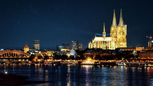 Illuminated buildings and cologne cathedral in city at night. 