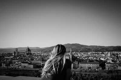 Rear view of woman looking at cityscape against clear sky