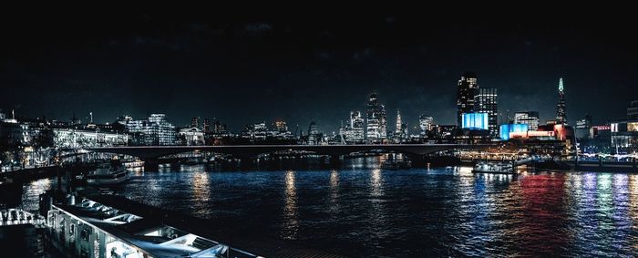 Illuminated buildings by river against sky in city at night