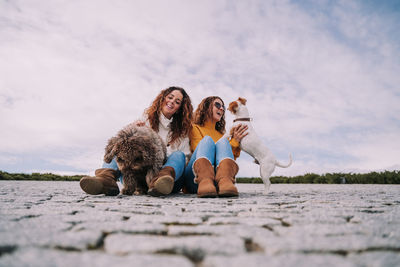 Female friends with dogs sitting on footpath