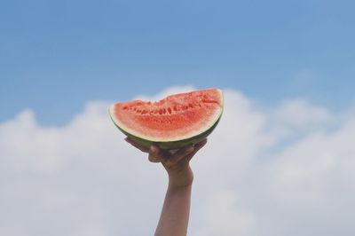 Close-up of hand holding strawberry against sky