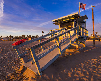 Deck chairs on beach against sky during sunset