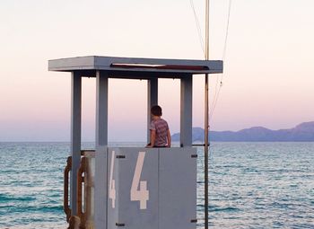 Rear view of boy sitting in lifeguard hut at beach