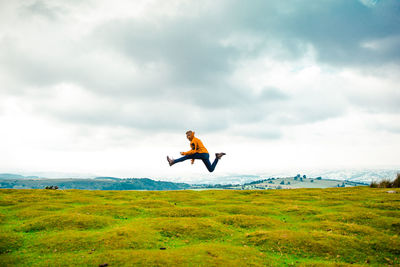 Side view of man jumping on grassy field against cloudy sky