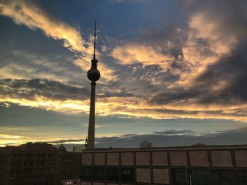 Communications tower in city against sky during sunset