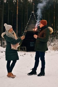 Full length of couple standing in snow holding sparklers