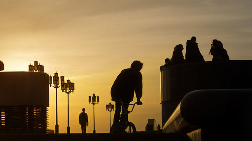 Silhouette people sitting by sea against sky during sunset