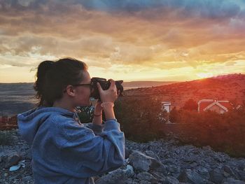 Woman photographing against sky during sunset