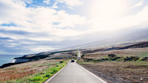 Road by landscape against cloudy sky