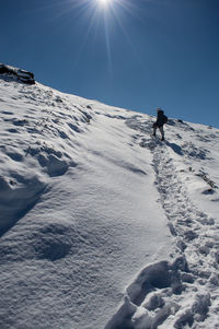 Person walking on snowcapped mountain against blue sky