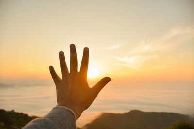 Cropped hand showing stop gesture towards sky at sunset