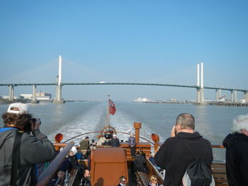 People in boat on thames river against clear blue sky in city