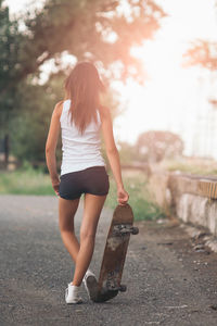 Rear view of woman standing with skateboard