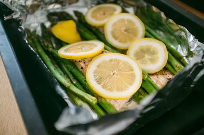 Close-up of lemon slices and asparagus with salmon on foil in container