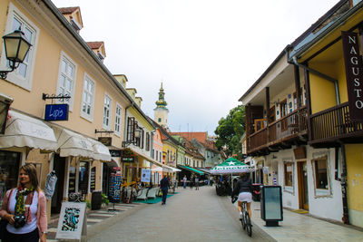 People on street amidst buildings against sky in city