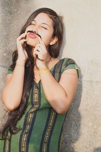 Smiling young woman making artificial mustache against wall