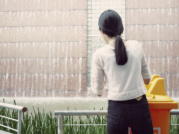 Rear view of woman standing against recycling bin and railing