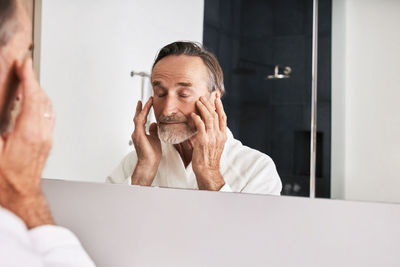 Senior man with closed eyes standing in front of mirror