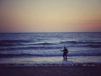 Silhouette man fishing at sea against sky during sunset