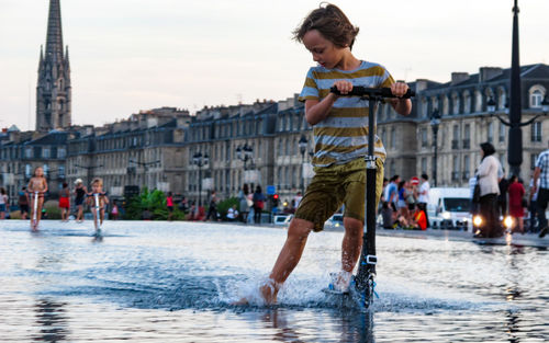 Full length of boy on water in city against sky