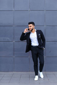 Full length of businessman talking on phone standing against wall