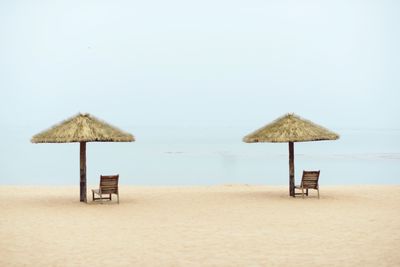 Lounge chairs by thatched roofs on sandy beach