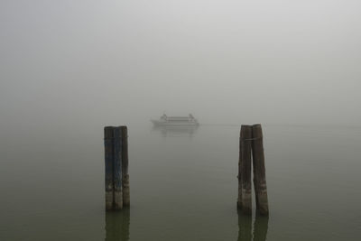 Wooden posts in sea against sky